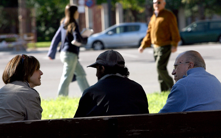 Dos voluntarios de Caritas hablan con una persona sin hogar en un parque de Valencia