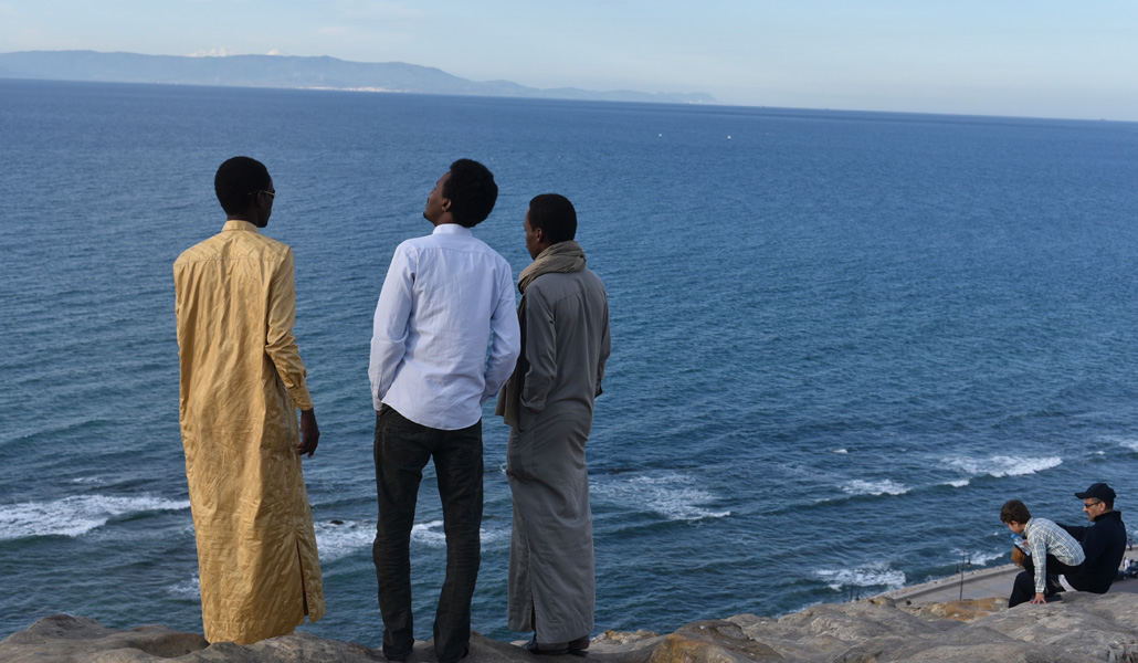 Tres jóvenes, en la costa de Tánger, contemplan a lo lejos España en junio de 2018