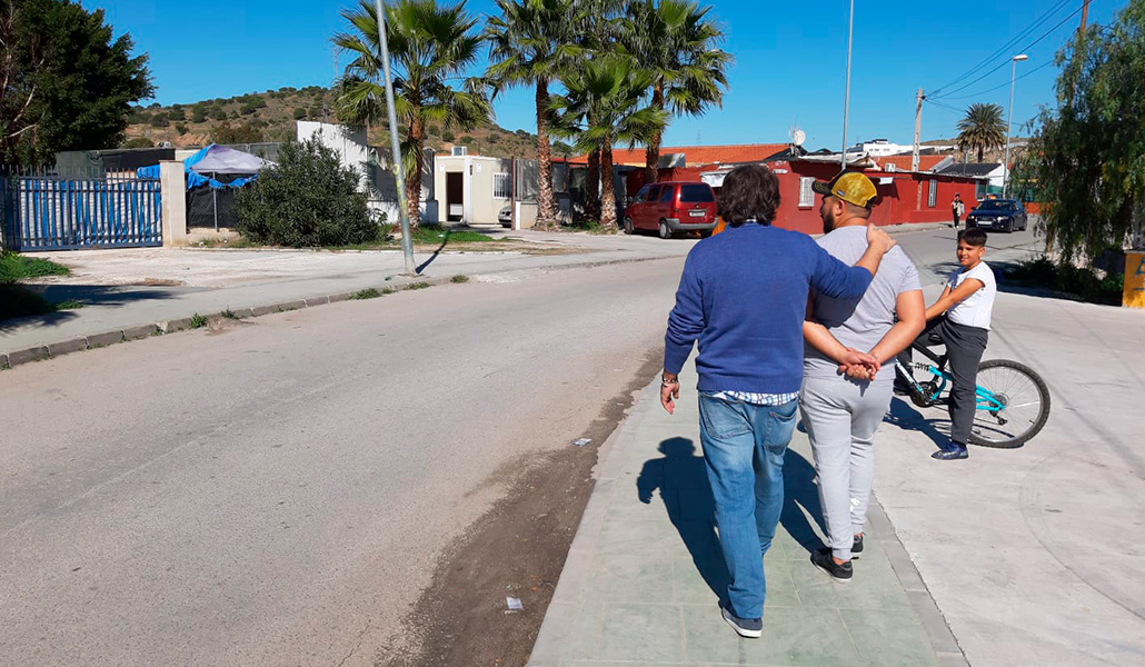 Un miembro del equipo de la Universidad de Málaga pasea con uno de los vecinos de Los Asperones y su hijo