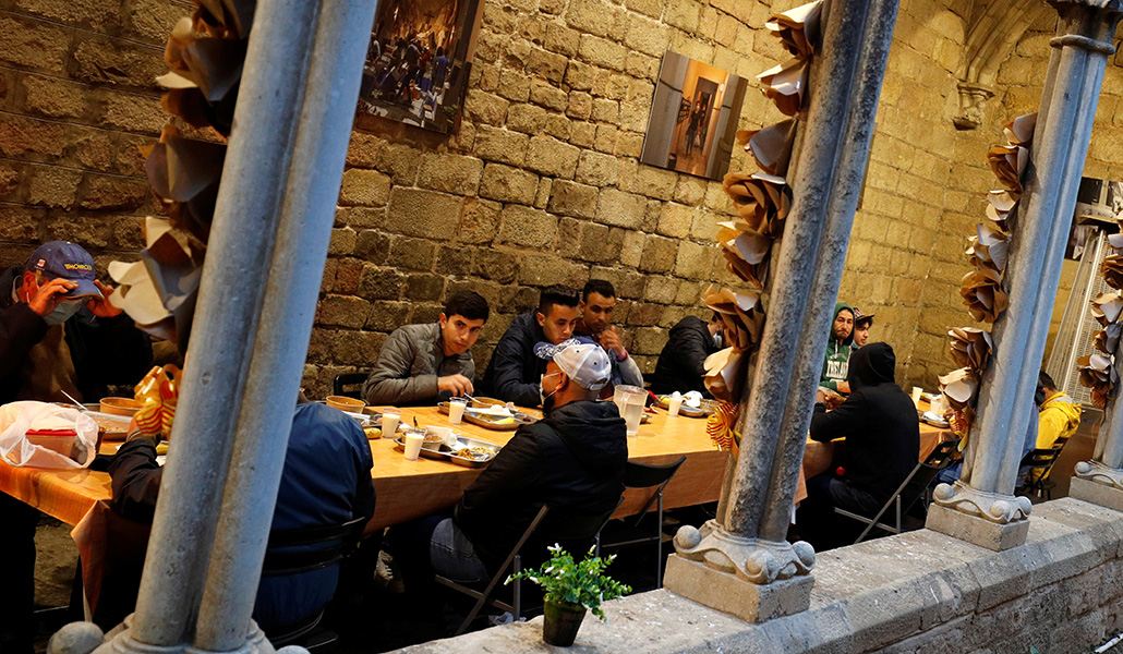 Un grupo de migrantes cena en el claustro de la iglesia de Santa Anna, en Barcelona, uno de los recursos que presenta la guía