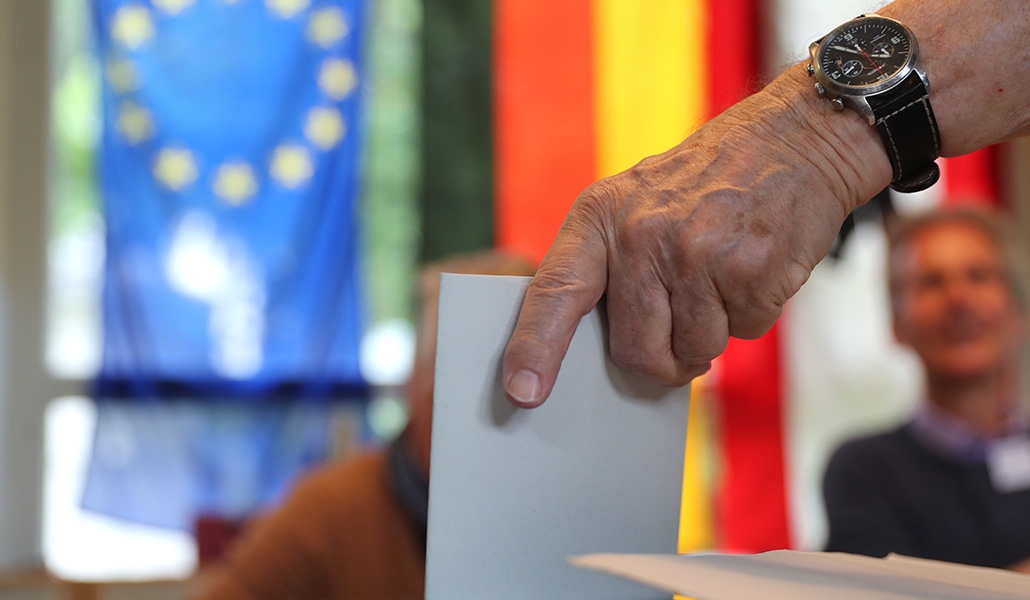 Una persona junto a una bandera de la Unión Europea y de Alemania, vota durante unas elecciones europeas