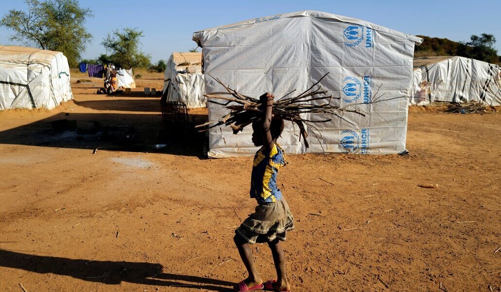 Una niña lleva leña en la cabeza en un campo de desplazados del Sahel.
