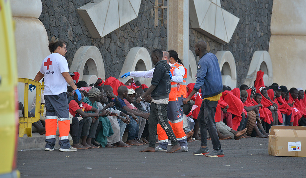 Trabajadores de la Cruz Roja al lado de los migrantes que han llegado en un cayuco al puerto de La Restinga, a 23 de octubre de 2023, en la isla de El Hierro