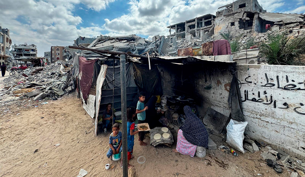 Mujeres y niños palestinos se sientan en una tienda de campaña improvisada junto a los escombros de una casa destruida en la ofensiva militar de Israel, en medio del conflicto en curso entre Israel y Hamás, en Khan Younis, en el sur de la Franja de Gaza, el 7 de octubre de 2024