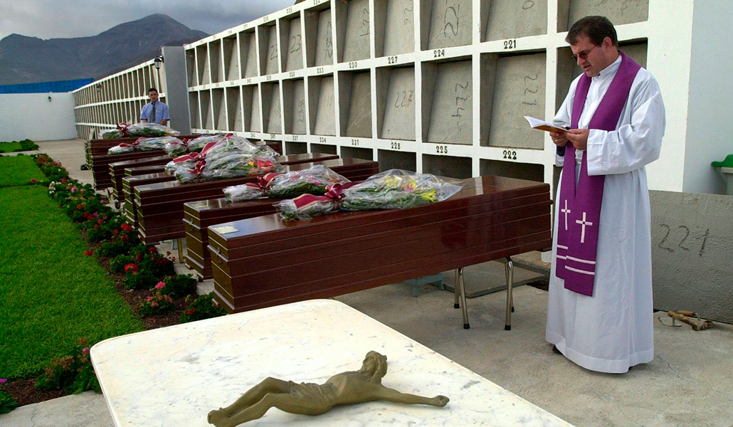 Un sacerdote reza un responso ante los féretros de un grupo de migrantes sin identificar