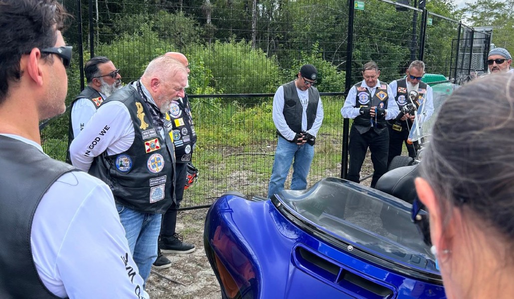 Wenski, con barba blanca, reza con los moteros al lado de la verja del recinto.