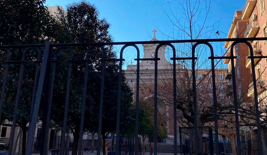 Una verja y árboles hacen difícil adivinar que detrás hay una iglesia.