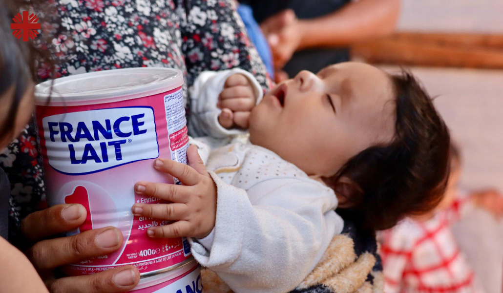 Un bebé dormido toca con su mano un bote de leche infantil.