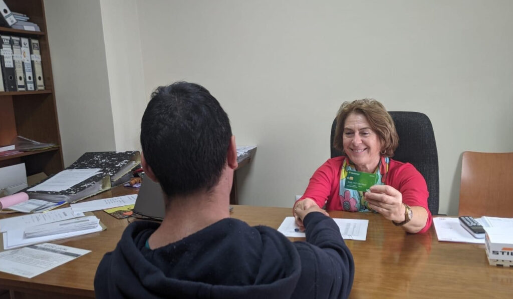 Una mujer saluda a un chico y le entrega una tarjeta.