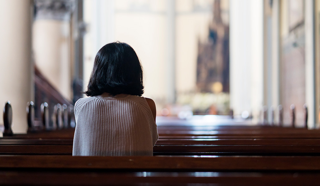 Foto de recurso de una mujer de espaldas en el banco de una iglesia