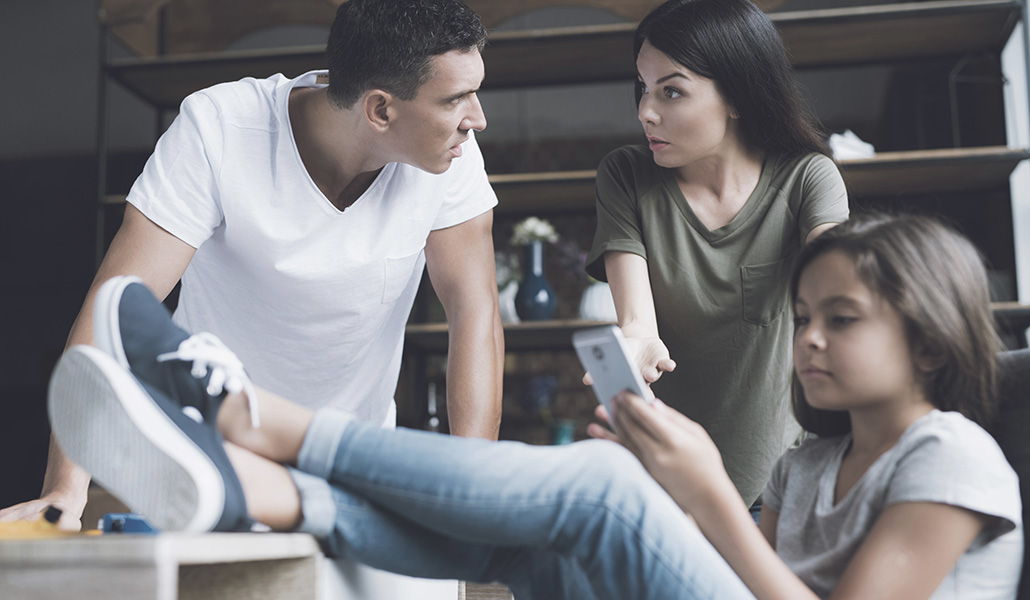Foto de recurso de unos padres con su hija adolescente que mira el móvil