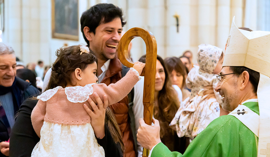Manuela en brazos de su madre y junto a su padre, agarra el báculo del cardenal durante la celebración.
