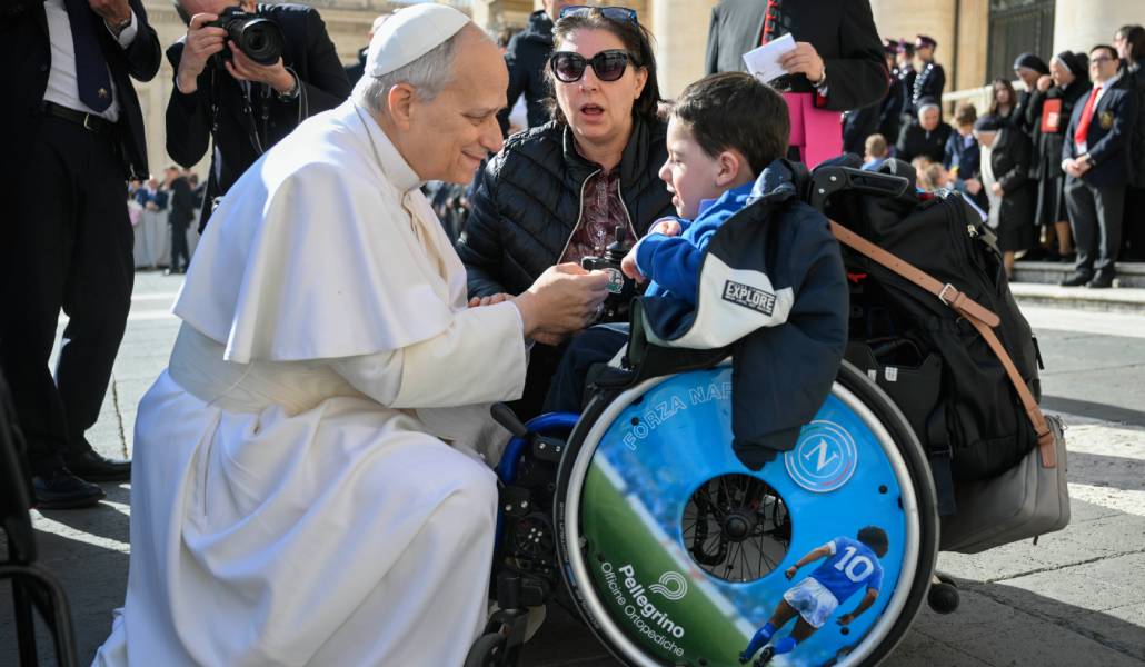 León XIV se arrodilla ante un niño en silla de ruedas durante una audiencia el pasado febrero. Foto: CNS.