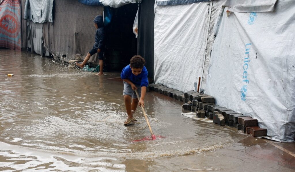 Un niño de Gaza intenta achicar el agua en torno a su refugio en noviembre pasado. Foto: OSV News / Reuters / Mahmoud Issa.